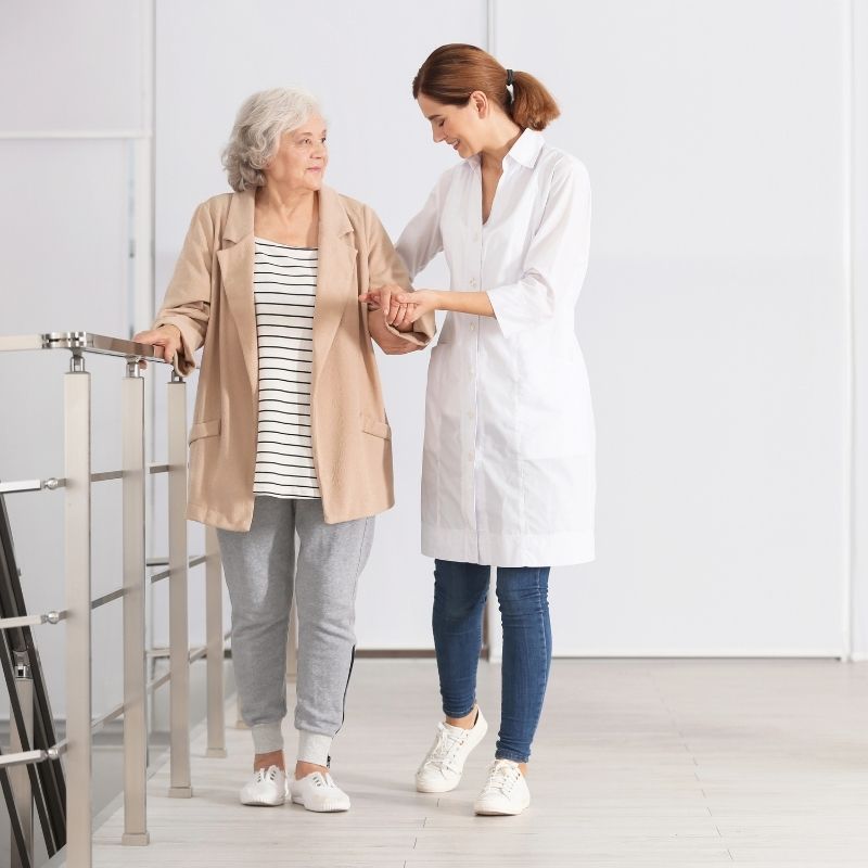 Elderly patient walking with a nurse during postoperative recovery following emergency surgery.